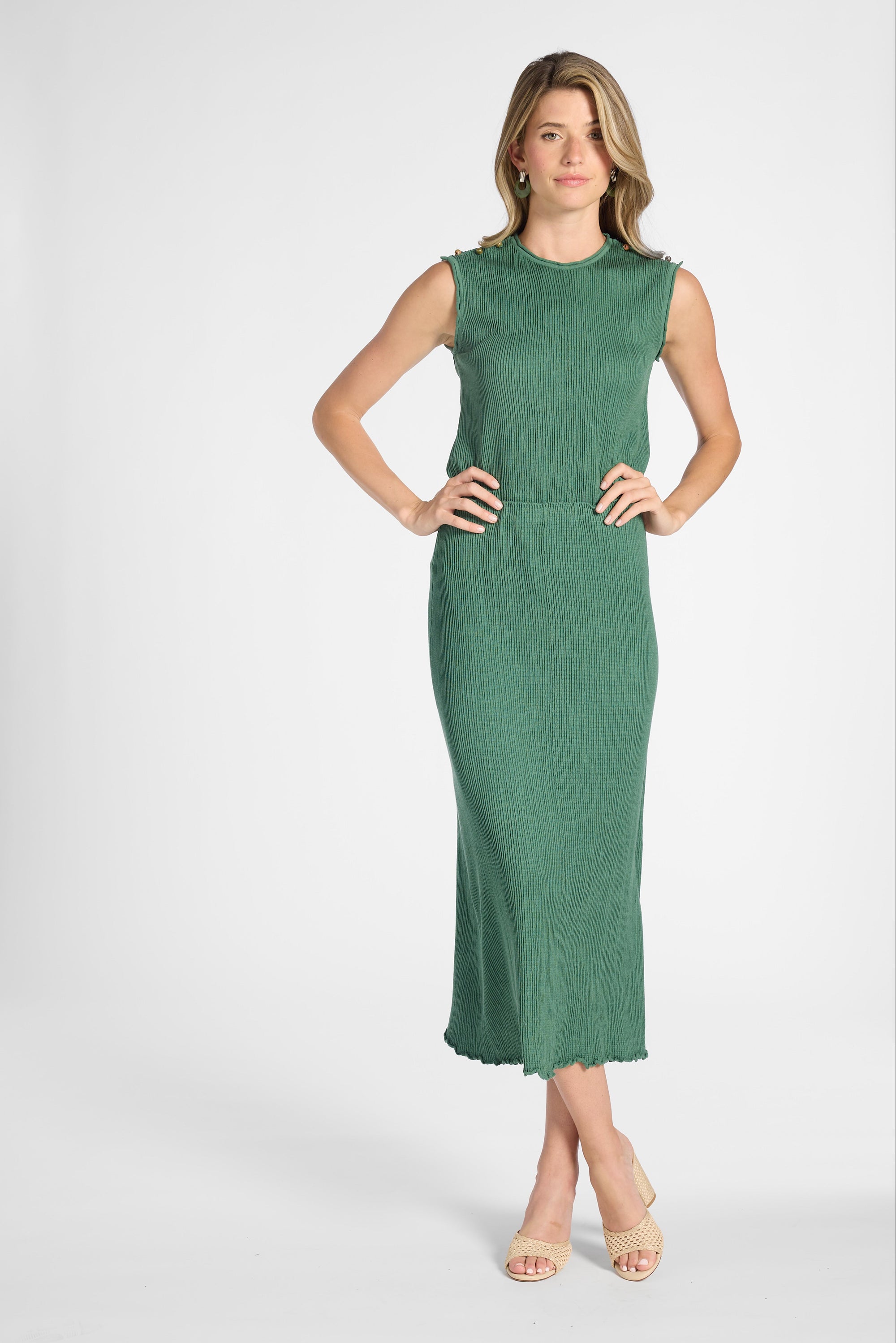 A woman modeling a sleeveless shell with a pleated skirt standing against a light gray studio background.