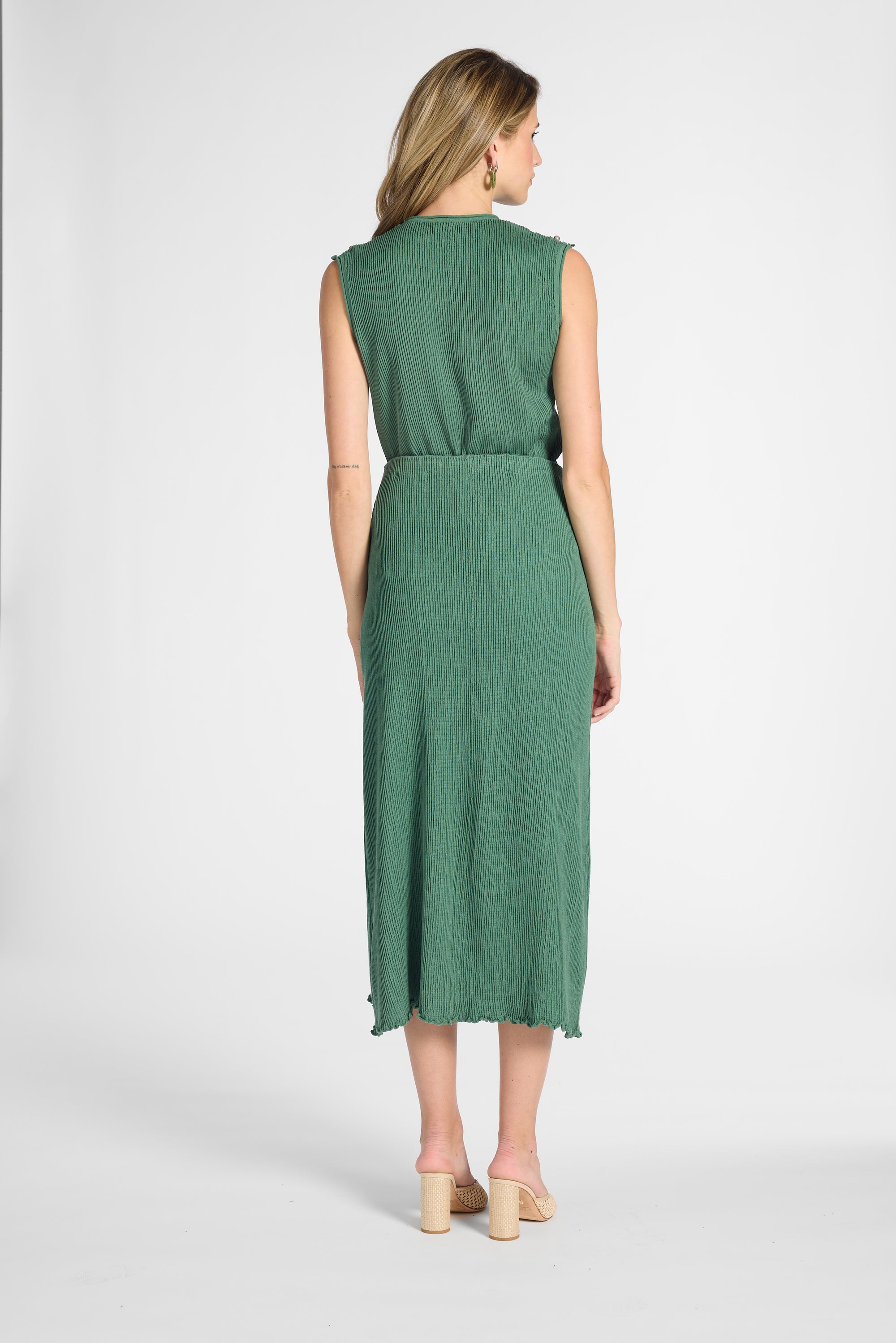 Woman standing wearing a pleated green shell with the matching green skirt on a white backdrop