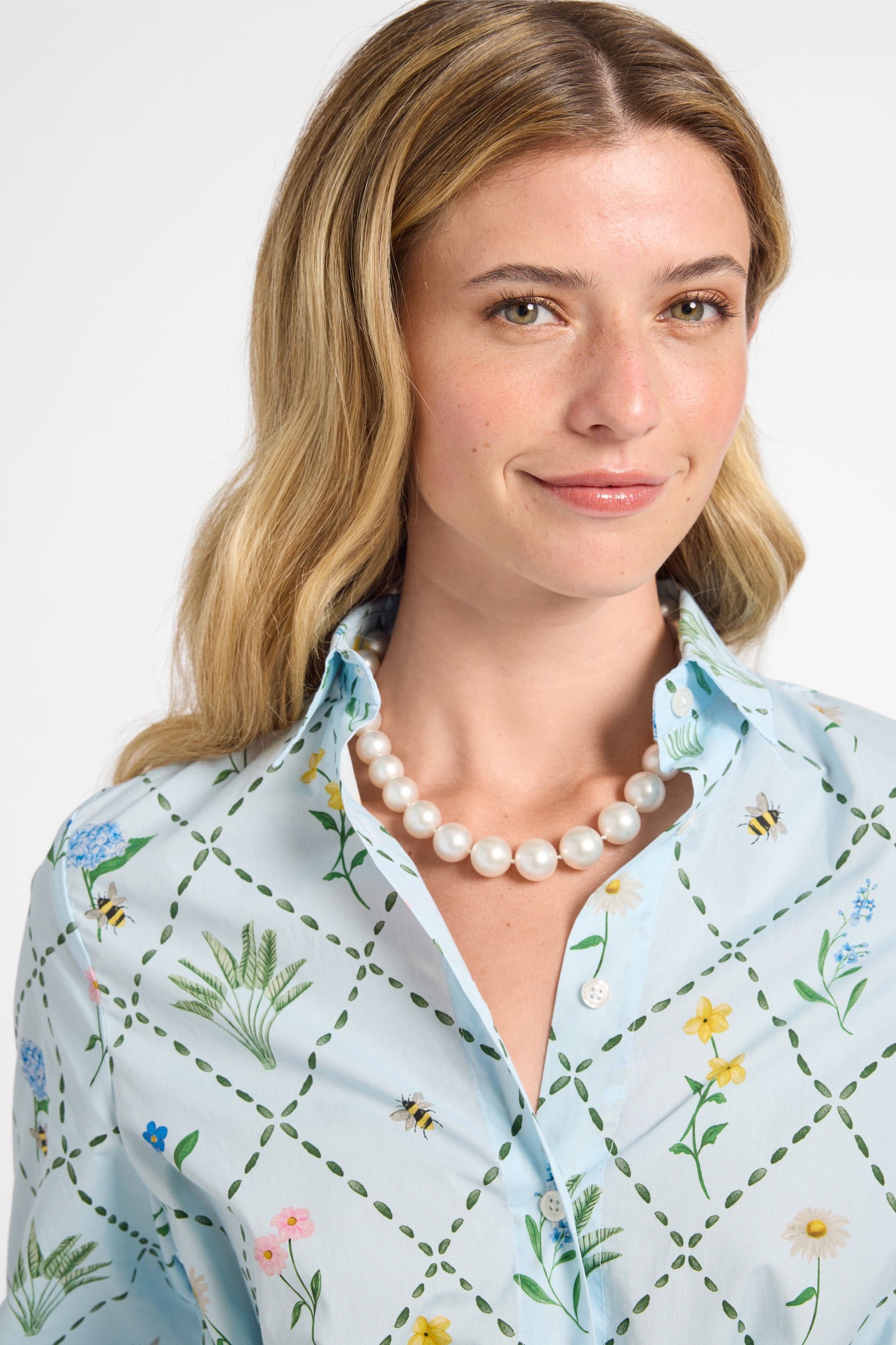 Woman wearing a light blue floral dress and pearls with a white background