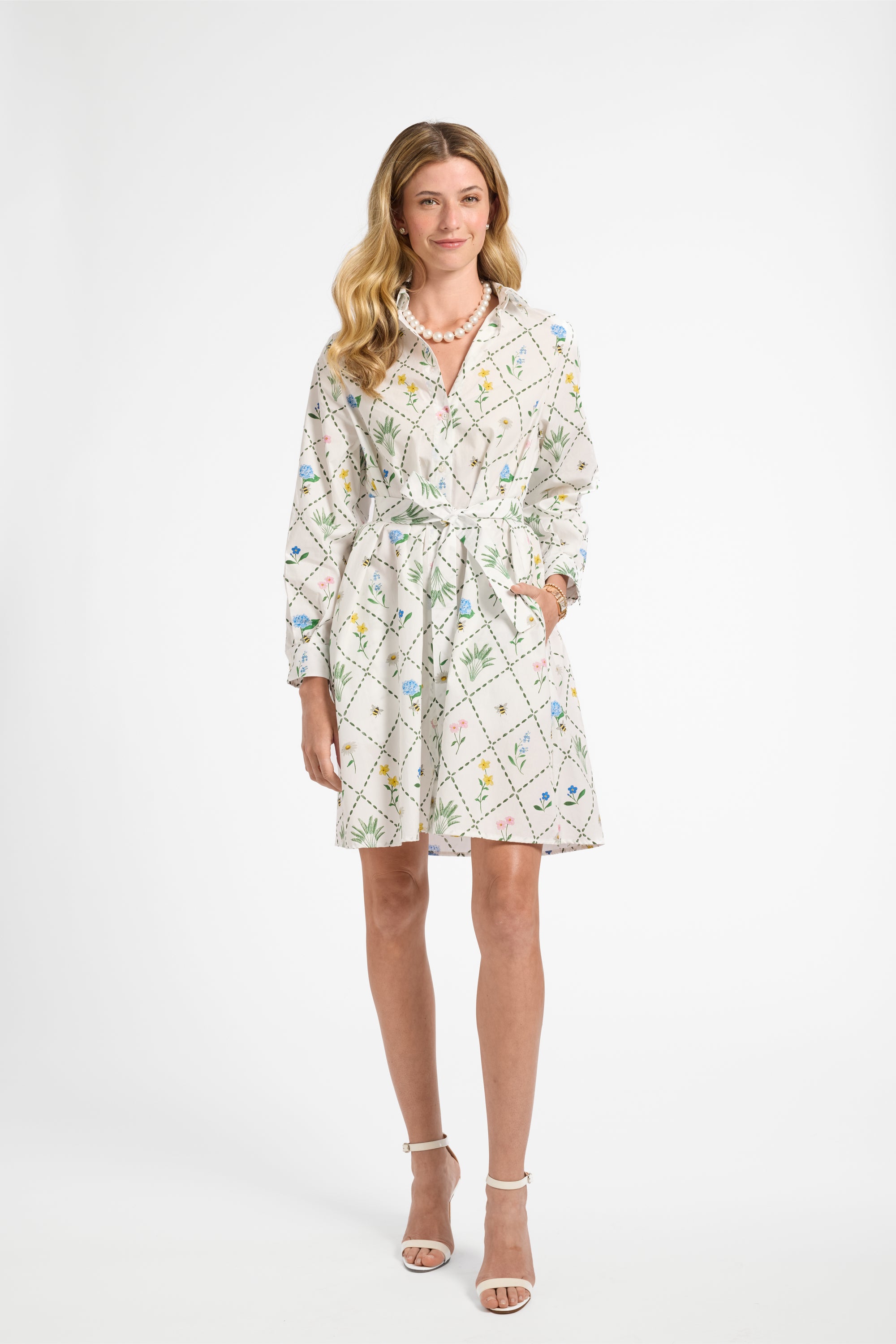 Woman modeling a mid-length white floral dress on a white backdrop