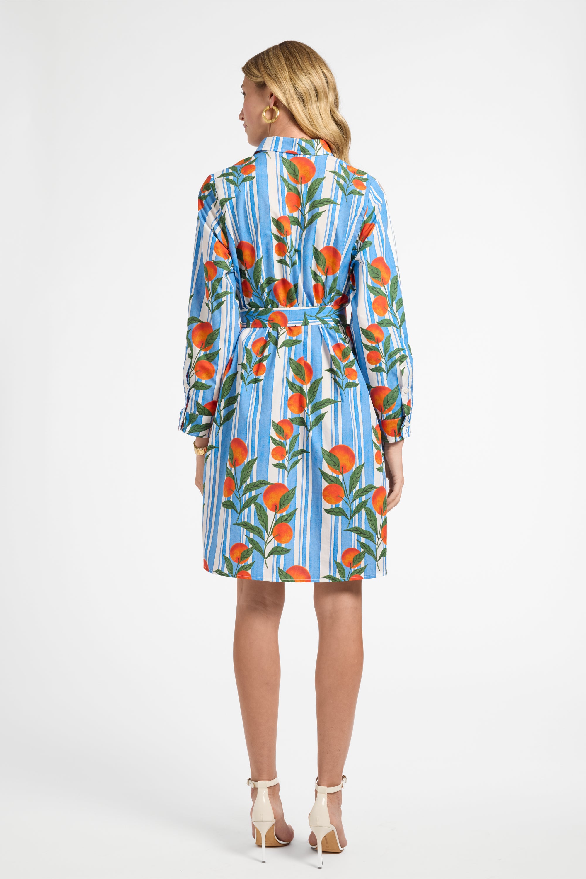 Woman modeling a blue striped dress with oranges on a plain backdrop