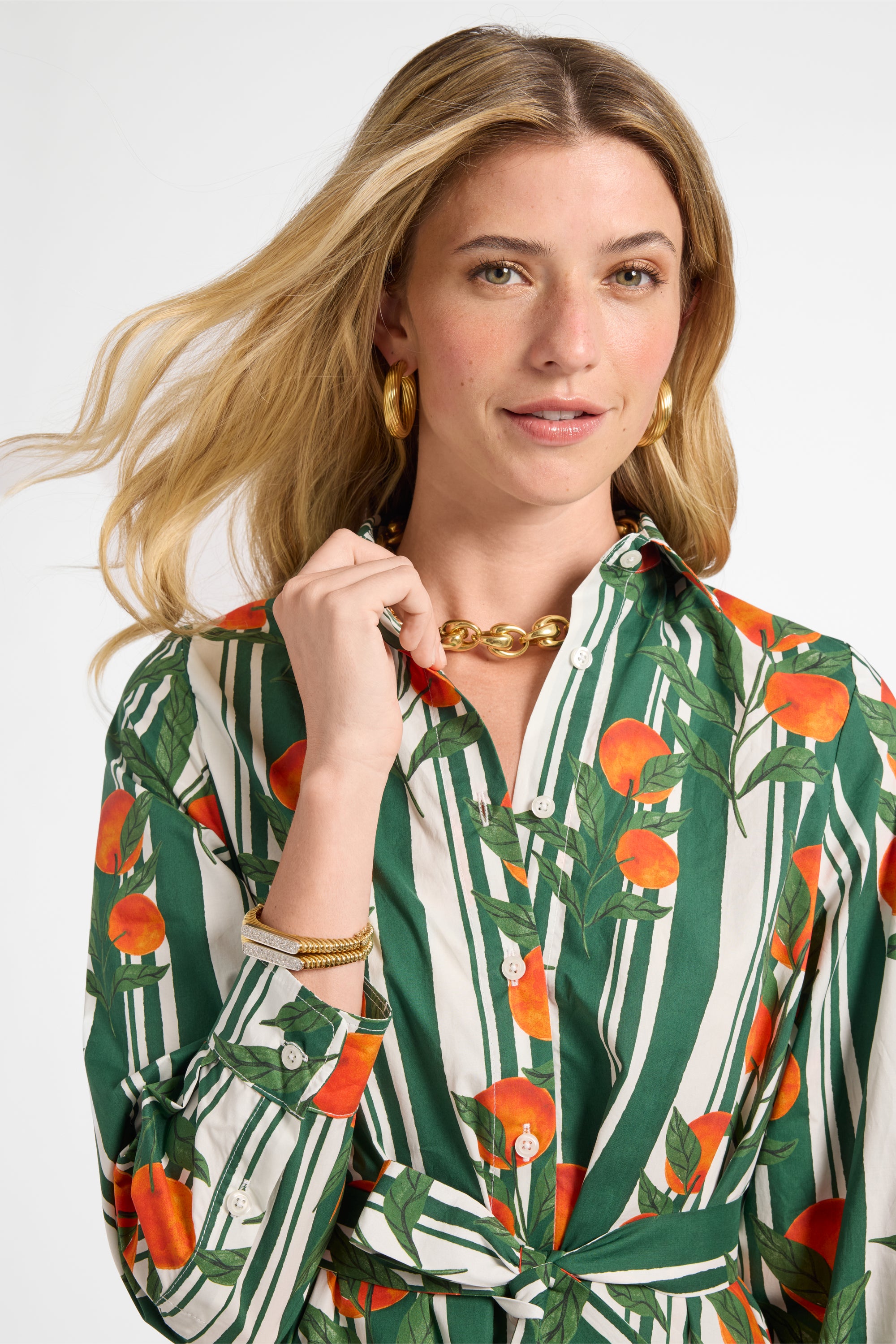 Woman wearing a patterned long sleeve dress with green, orange, and white design on a plain background