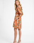 Woman modeling an orange and white striped dress with a fruit pattern on a plain backdrop