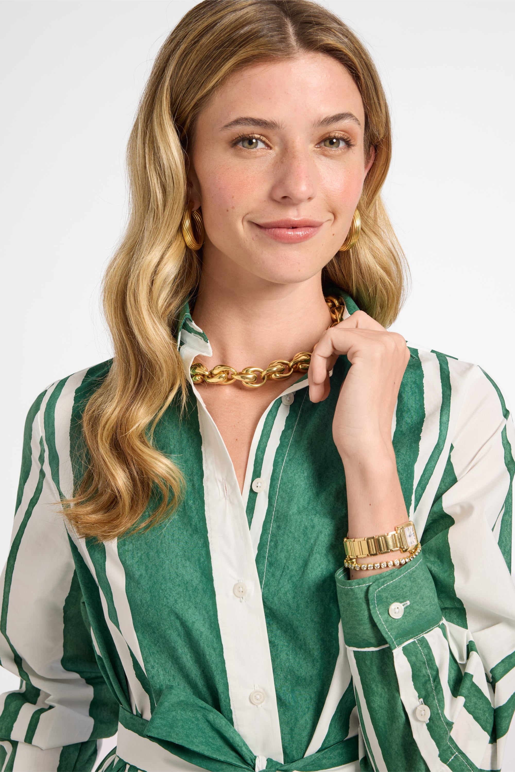 Woman wearing a green and white striped dress with gold jewelry on a plain background