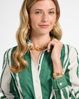 Woman wearing a green and white striped dress with gold jewelry on a plain background