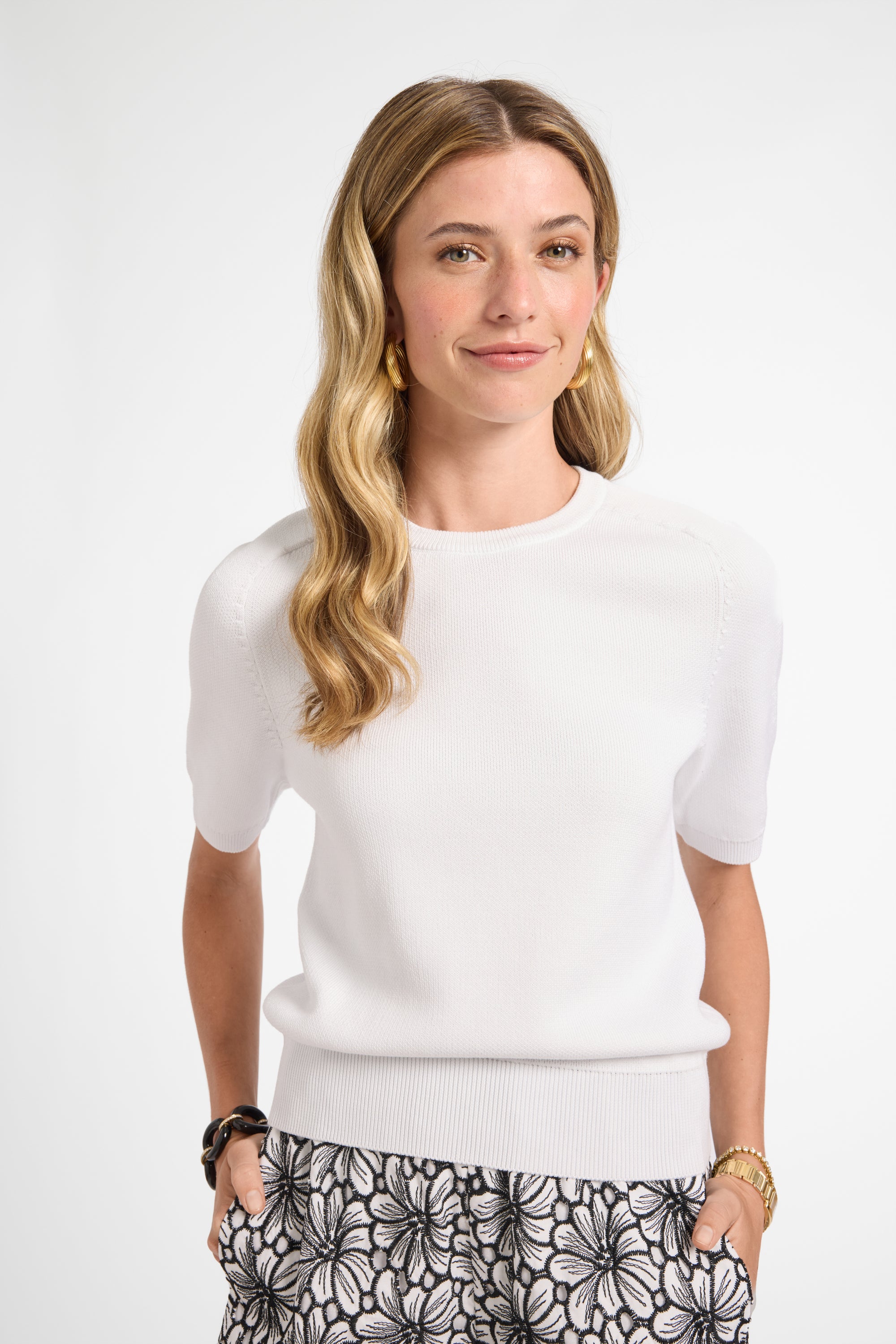 Woman wearing a white sweater and floral patterned pants on a white background