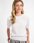 Woman wearing a white sweater and floral patterned pants on a white background
