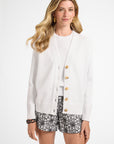 Woman wearing a white cardigan with buttons and black floral shorts on a white background