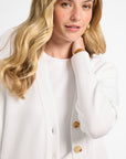 Woman wearing a white cardigan with buttons on a plain background