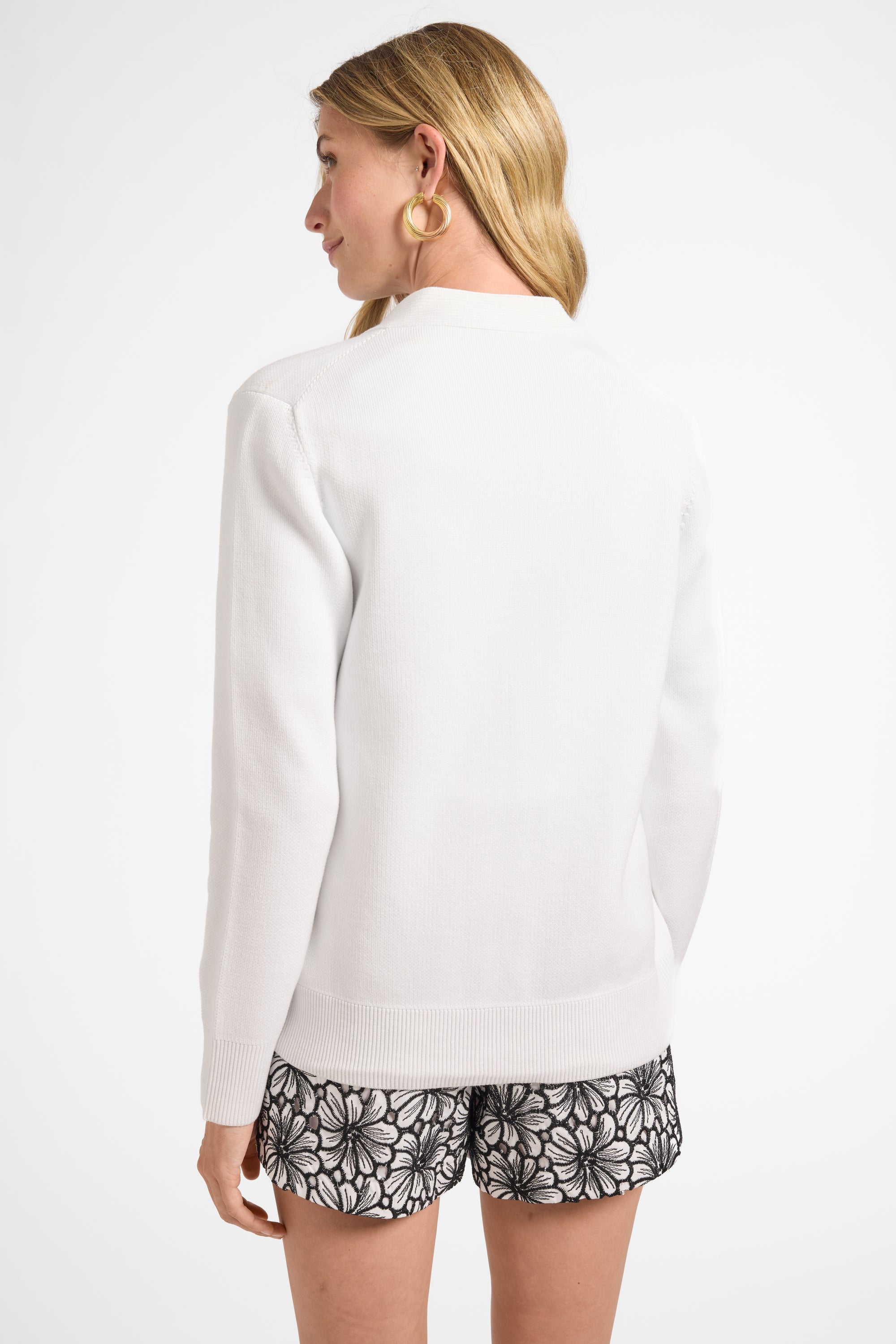 Woman wearing a white long-sleeve cardigan and patterned shorts on a white background