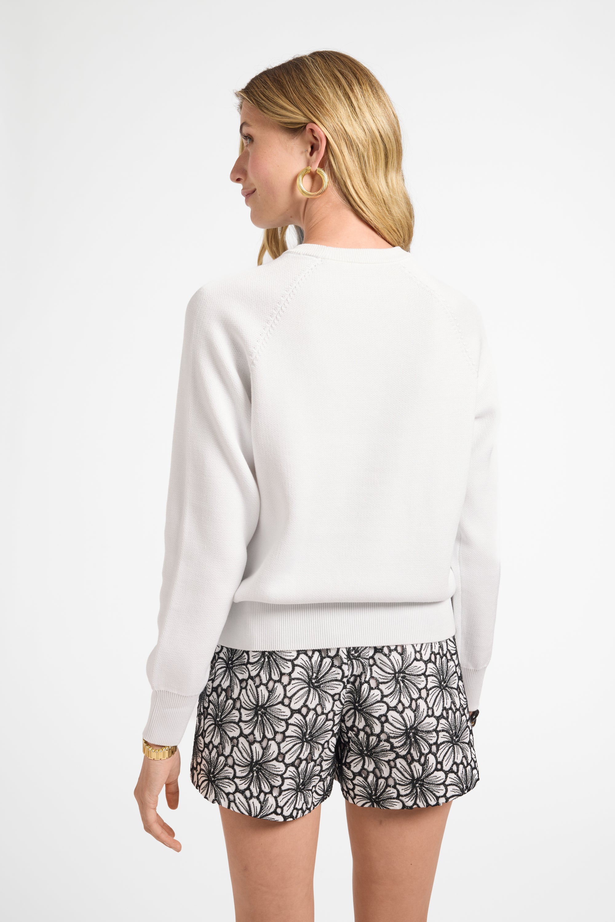 Woman modeling a long sleeve white sweater and patterned shorts on a white background