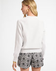 Woman modeling a long sleeve white sweater and patterned shorts on a white background