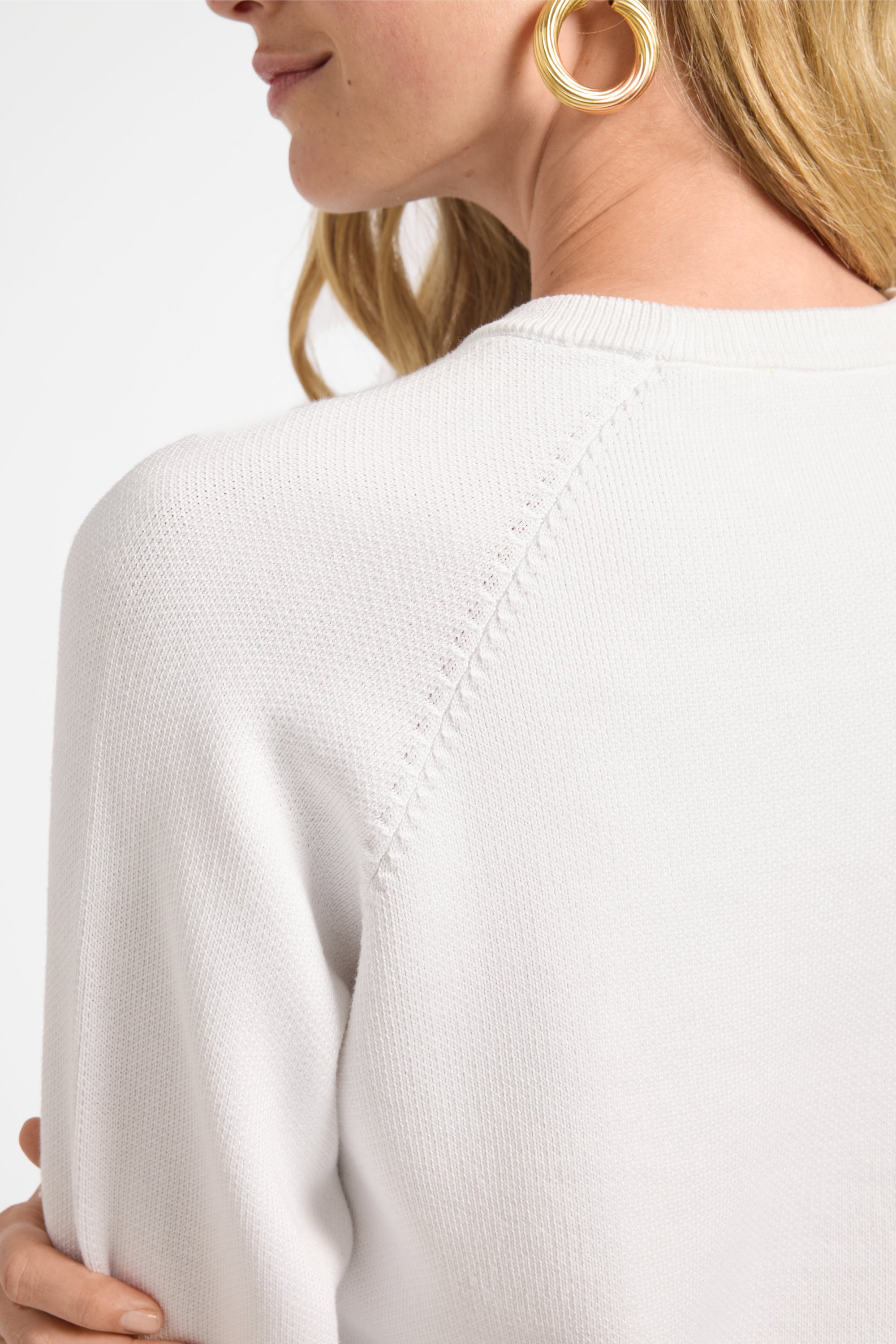 Close-up of a person wearing a white crewneck sweater with a plain background
