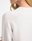 Close-up of a person wearing a white crewneck sweater with a plain background