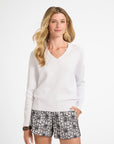 Woman wearing a white long-sleeve sweater and black floral shorts on a white background