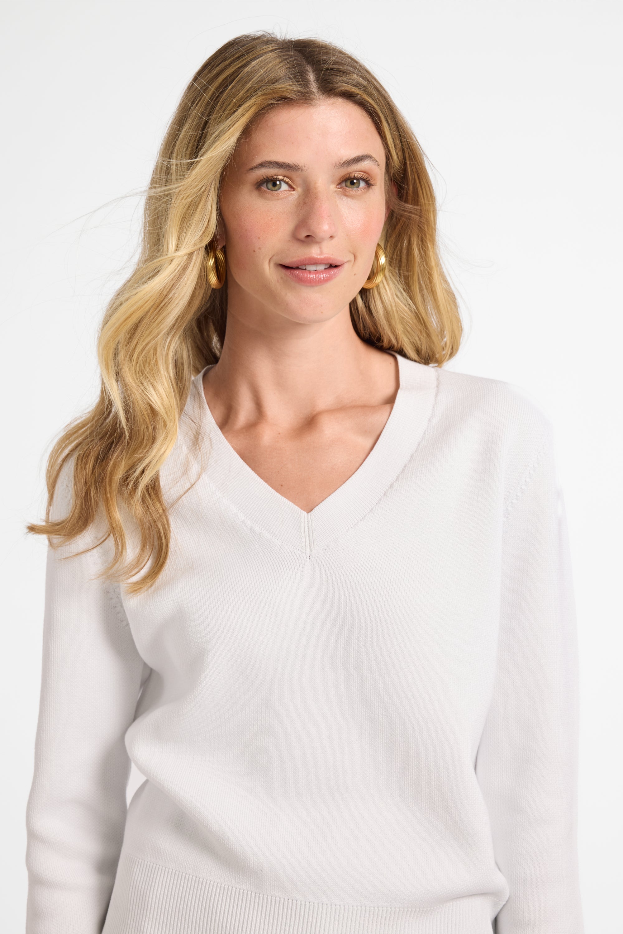 Woman wearing a white v-neck sweater against a plain background