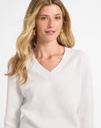 Woman wearing a white v-neck sweater against a plain background