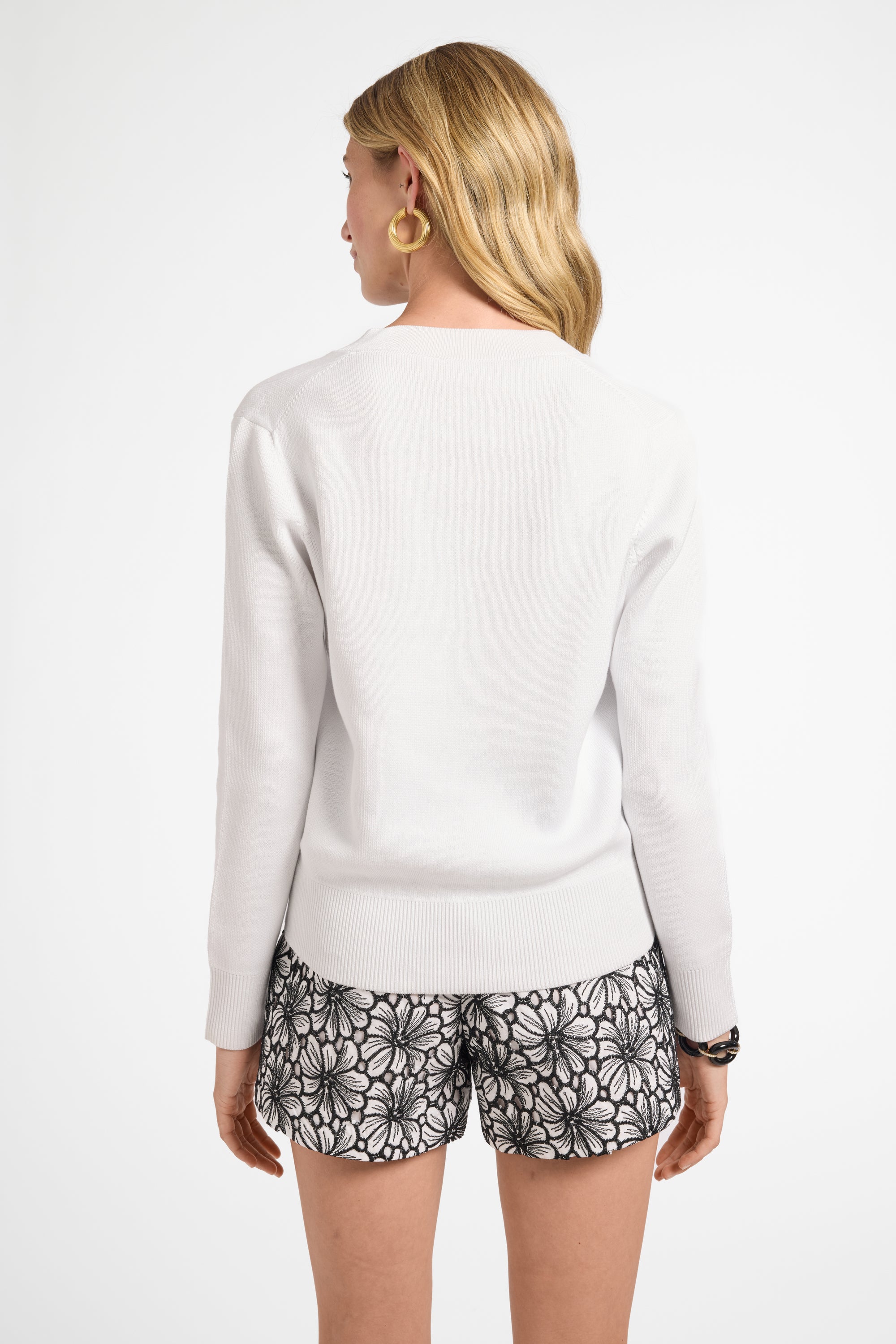 Woman wearing a white long-sweater top and patterned shorts on a white background