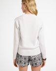 Woman wearing a white long-sweater top and patterned shorts on a white background