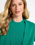 Woman wearing a green cardigan and shirt with a plain background