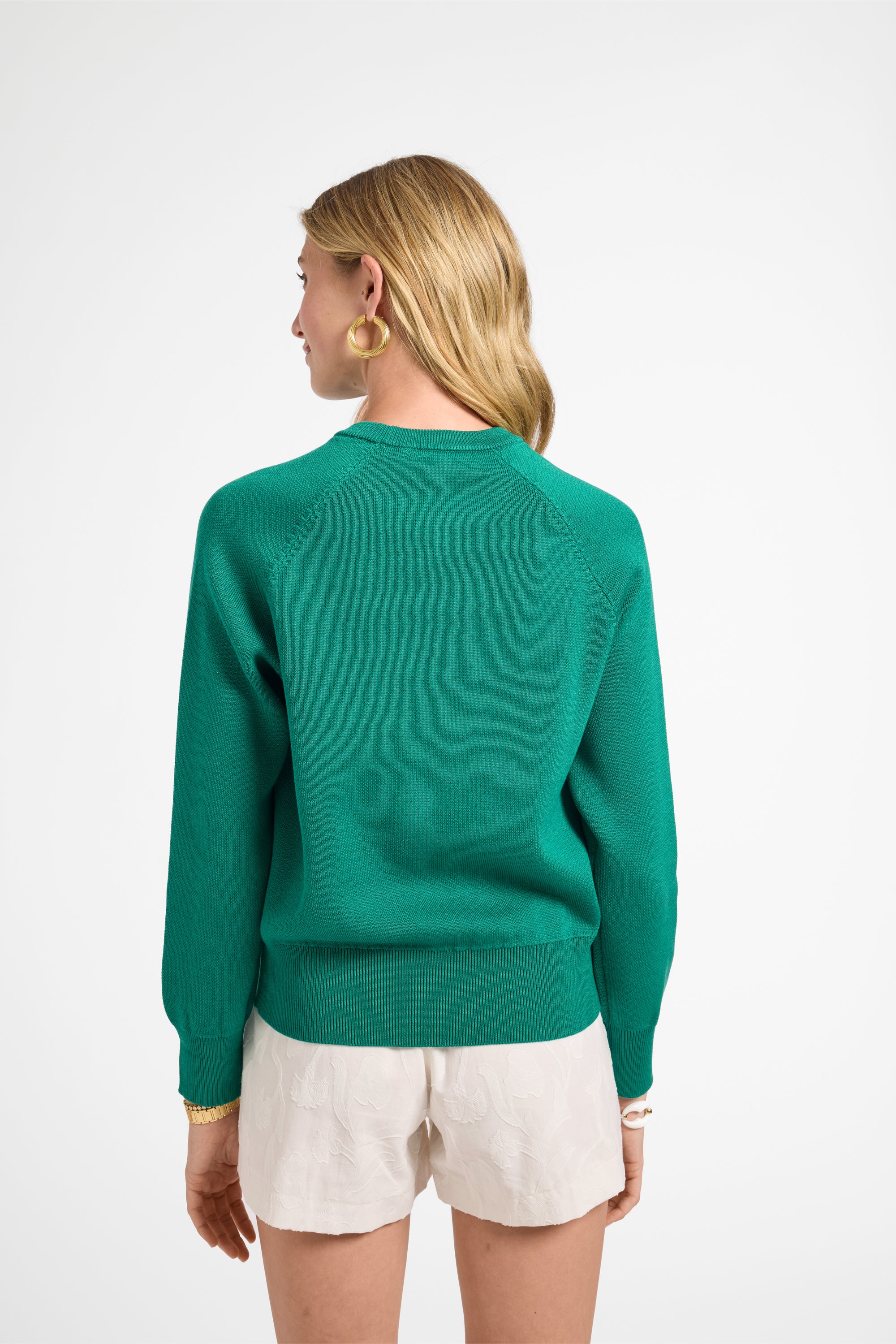 Woman wearing a green crewneck and white shorts on a white backdrop