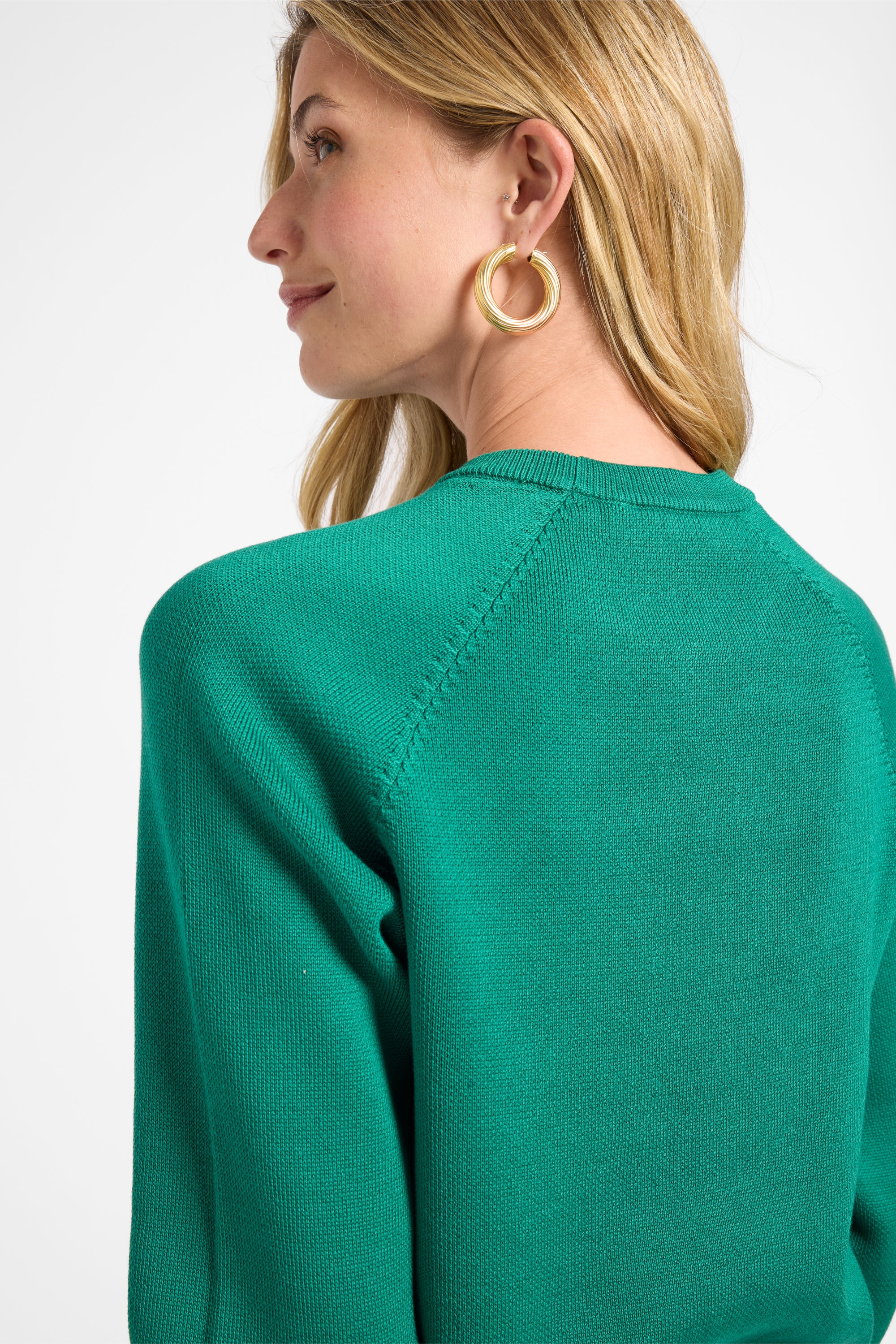 Woman wearing a green sweater with gold jewelry on a white background