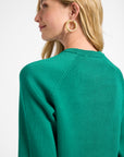 Woman wearing a green sweater with gold jewelry on a white background