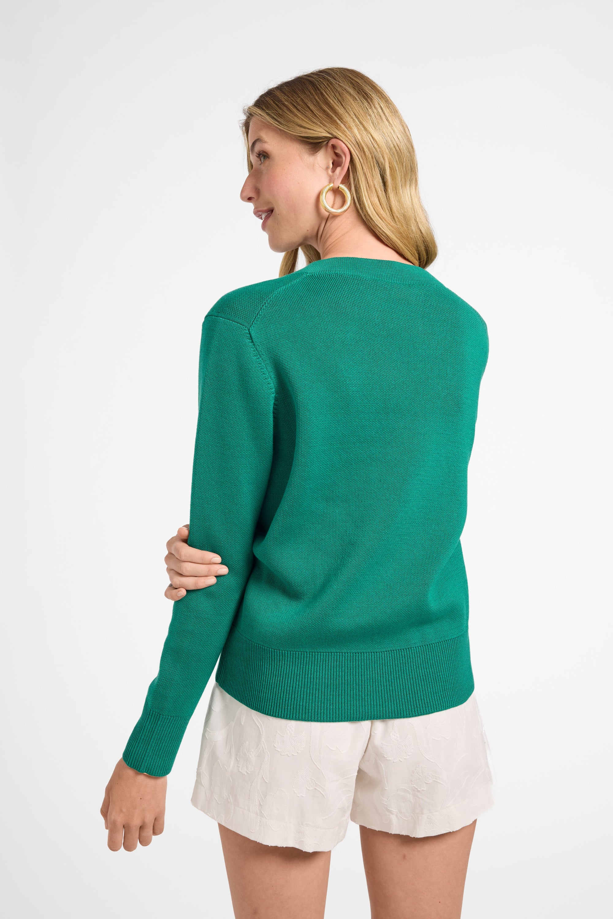 Woman wearing a green sweater and white shorts on a white background