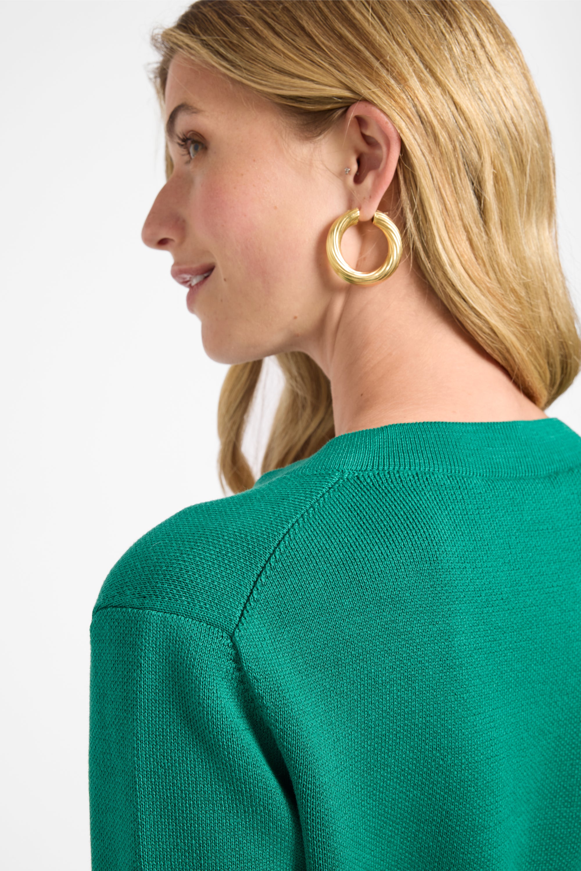 Woman wearing gold hoop earrings with a green sweater on a white background