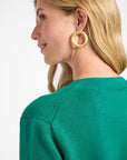 Woman wearing gold hoop earrings with a green sweater on a white background