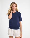 Woman wearing a navy sweater shirt and white shorts on a white background