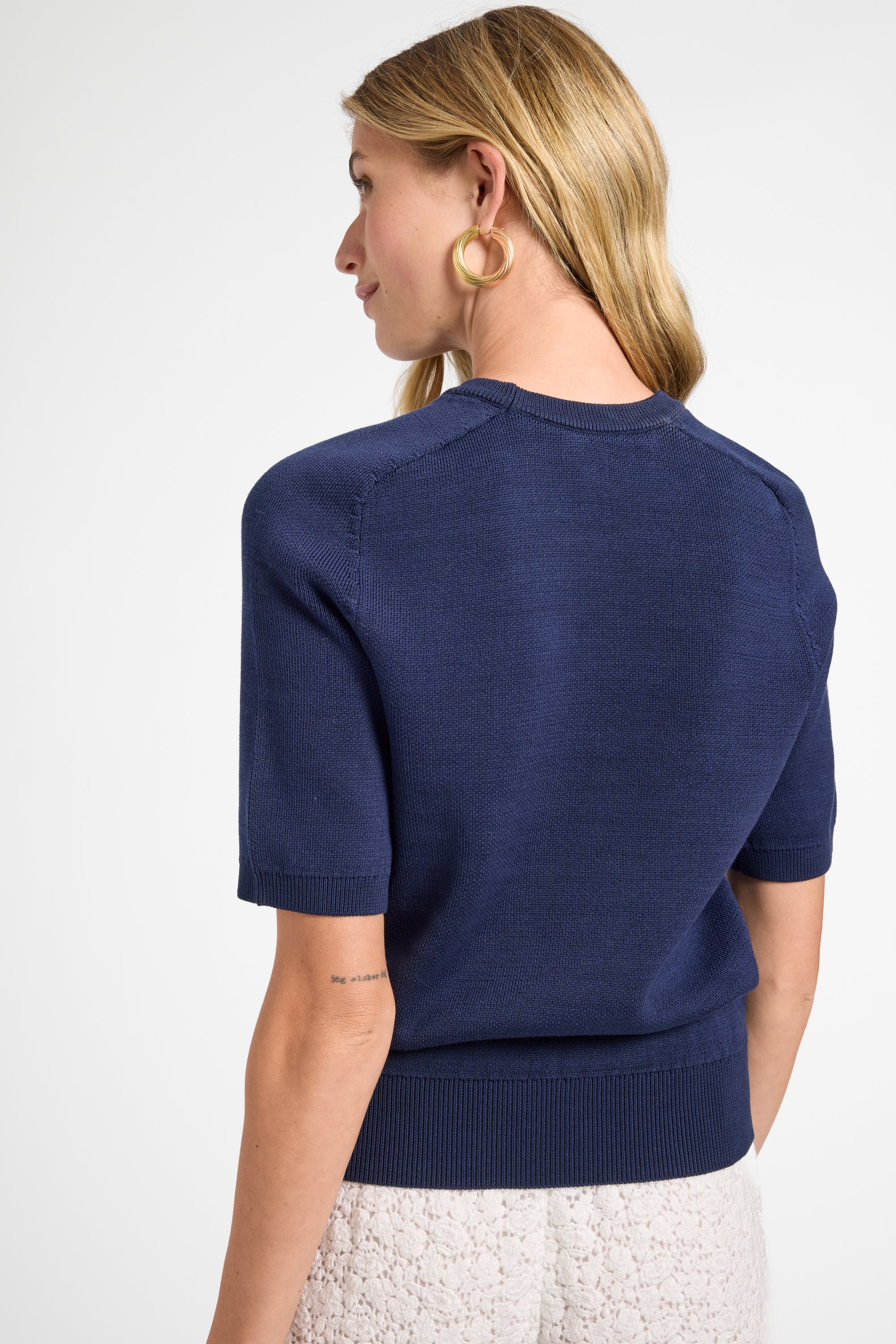 Woman wearing a navy blue top with gold hoops on a white background
