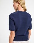 Woman wearing a navy blue top with gold hoops on a white background