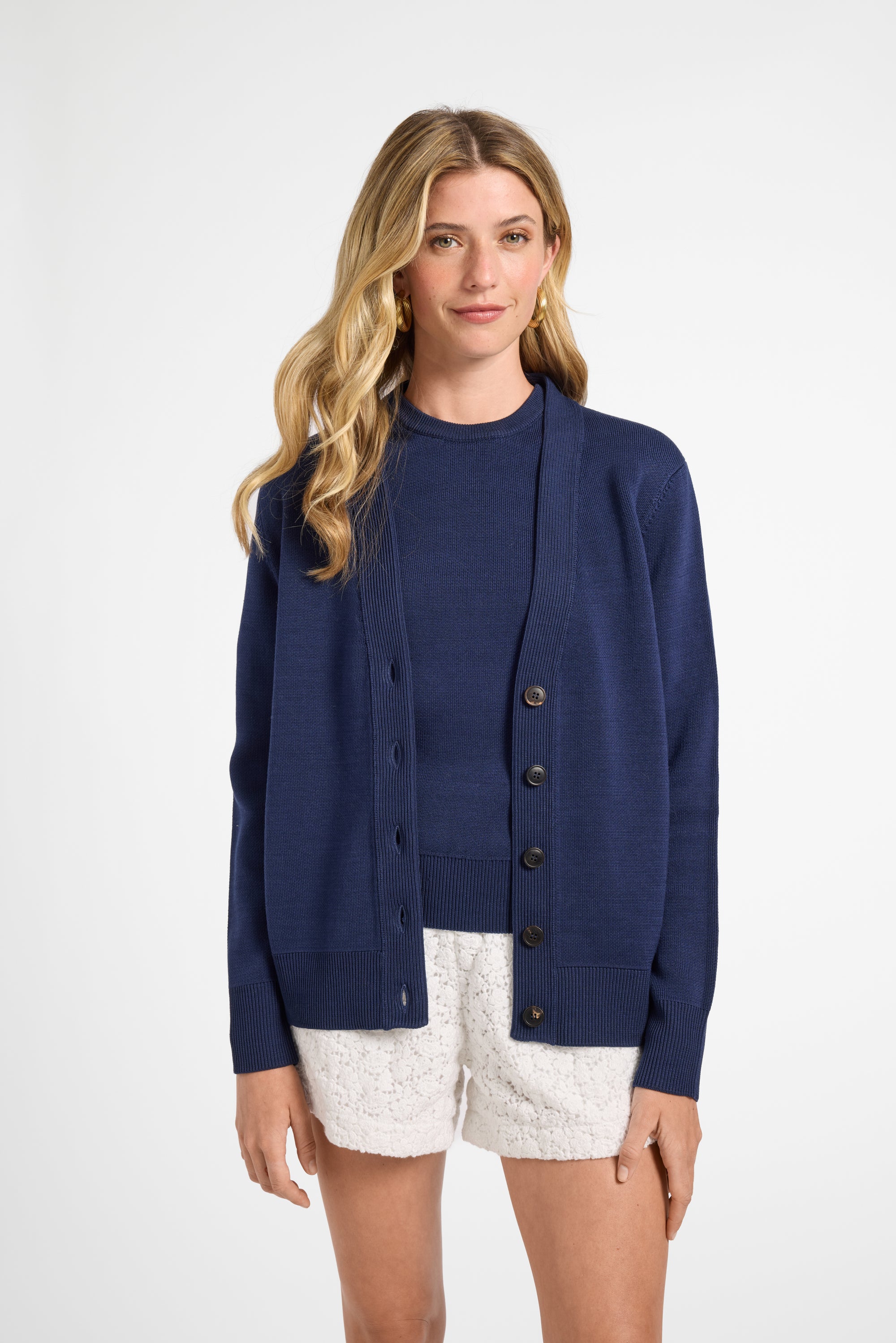 Woman wearing a blue cardigan over a white top and shorts on a white background