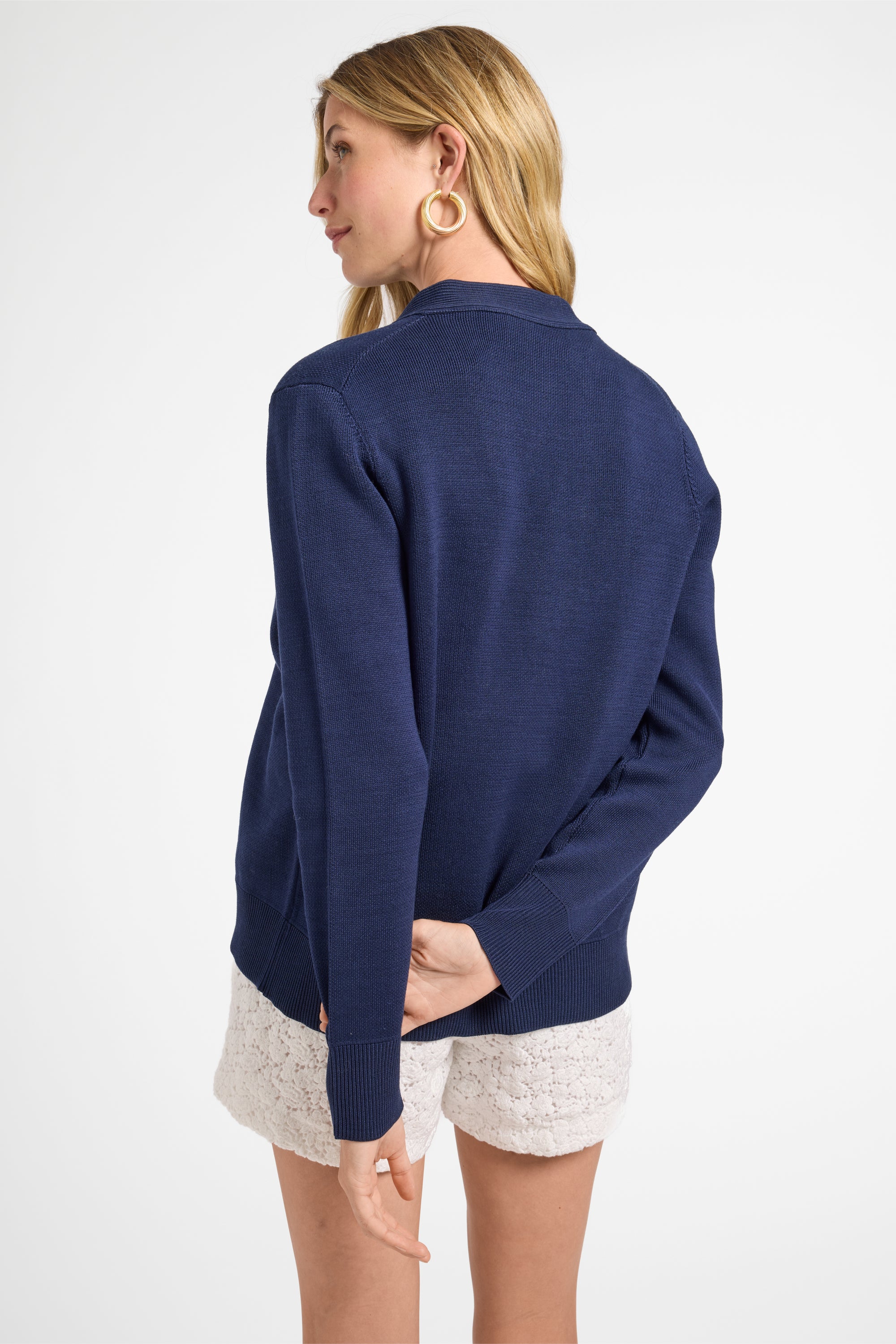 Woman wearing a navy cardigan sweater and white shorts on a white backdrop