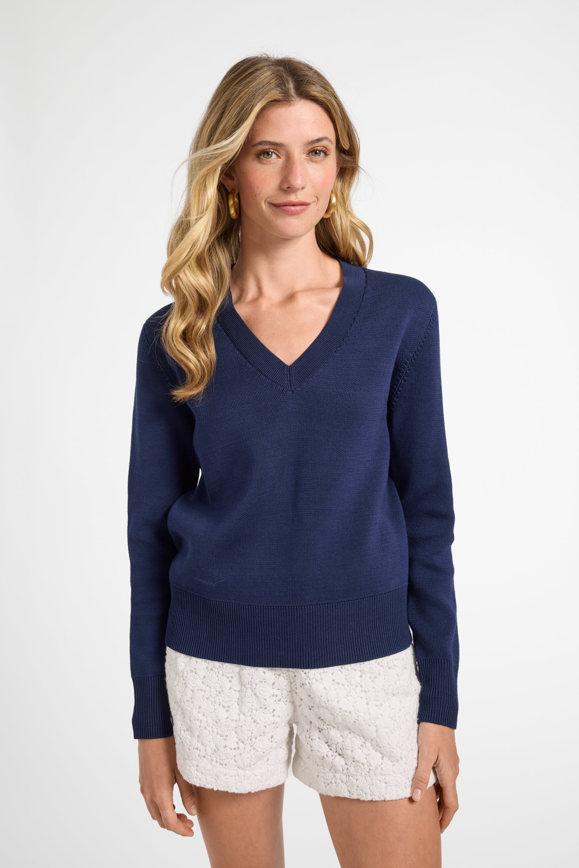 Woman wearing a navy blue sweater and white shorts on a white background