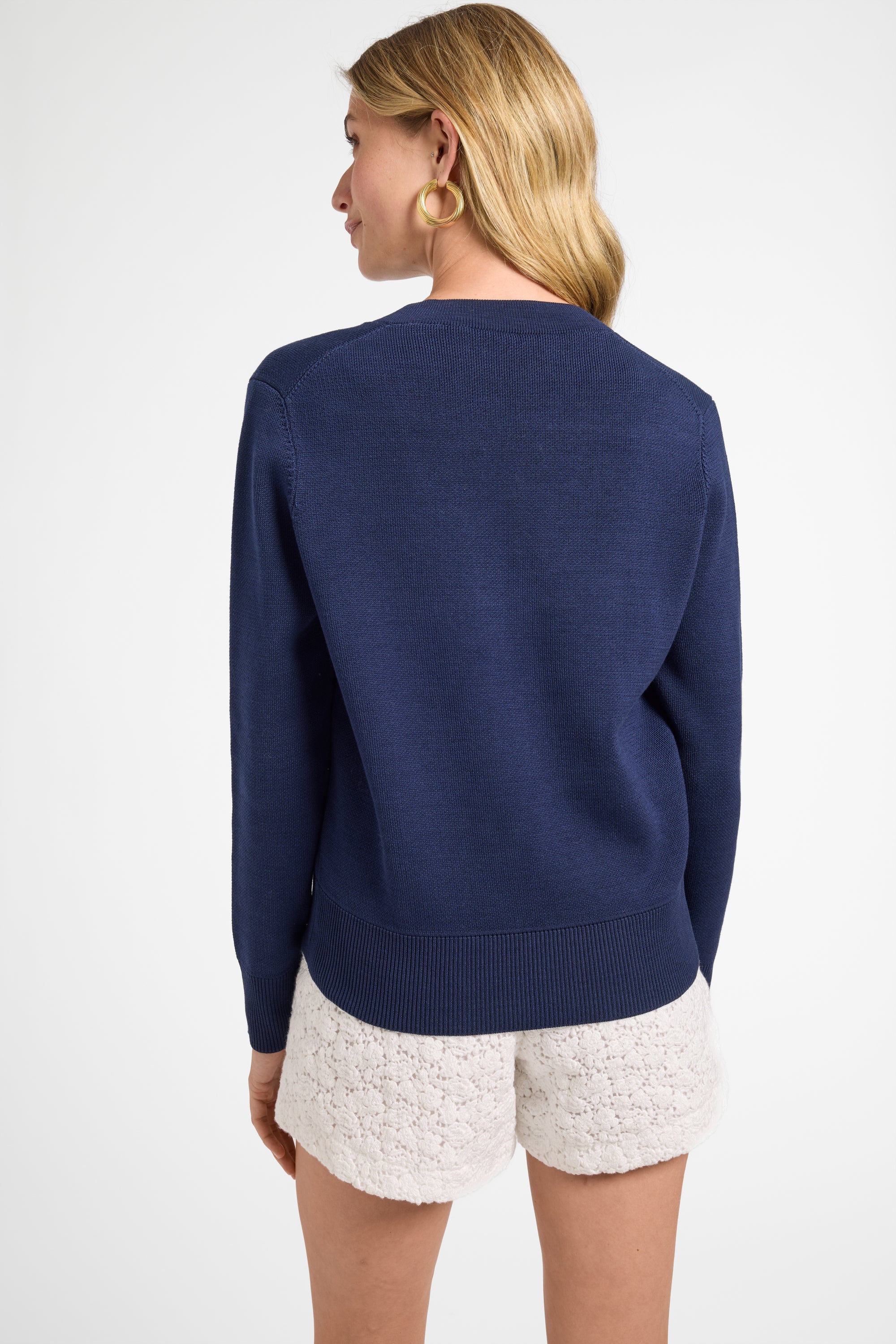 Woman wearing a long sleeve blue sweater and white shorts on a plain background