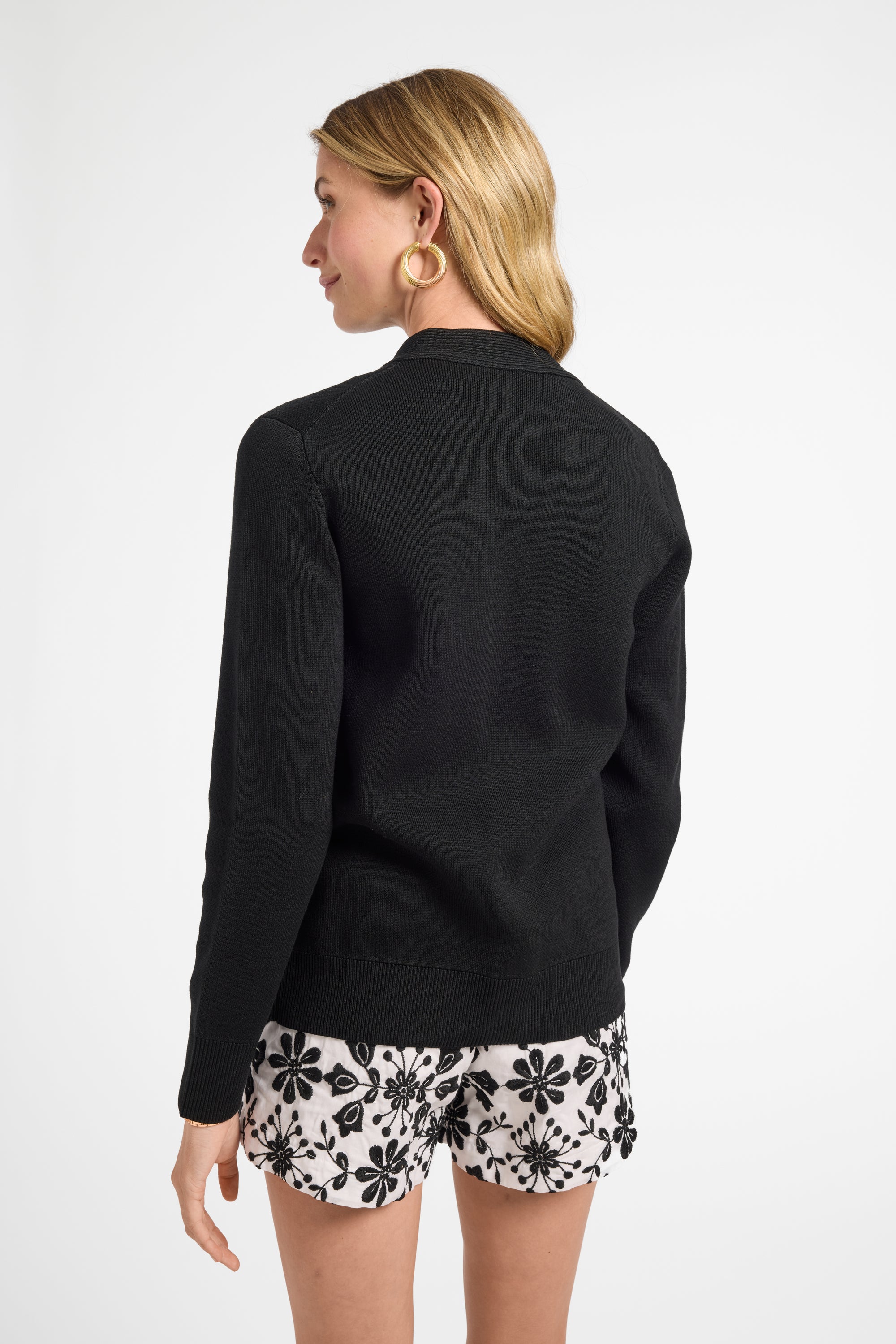 Woman wearing a black cardigan and floral shorts on a white background
