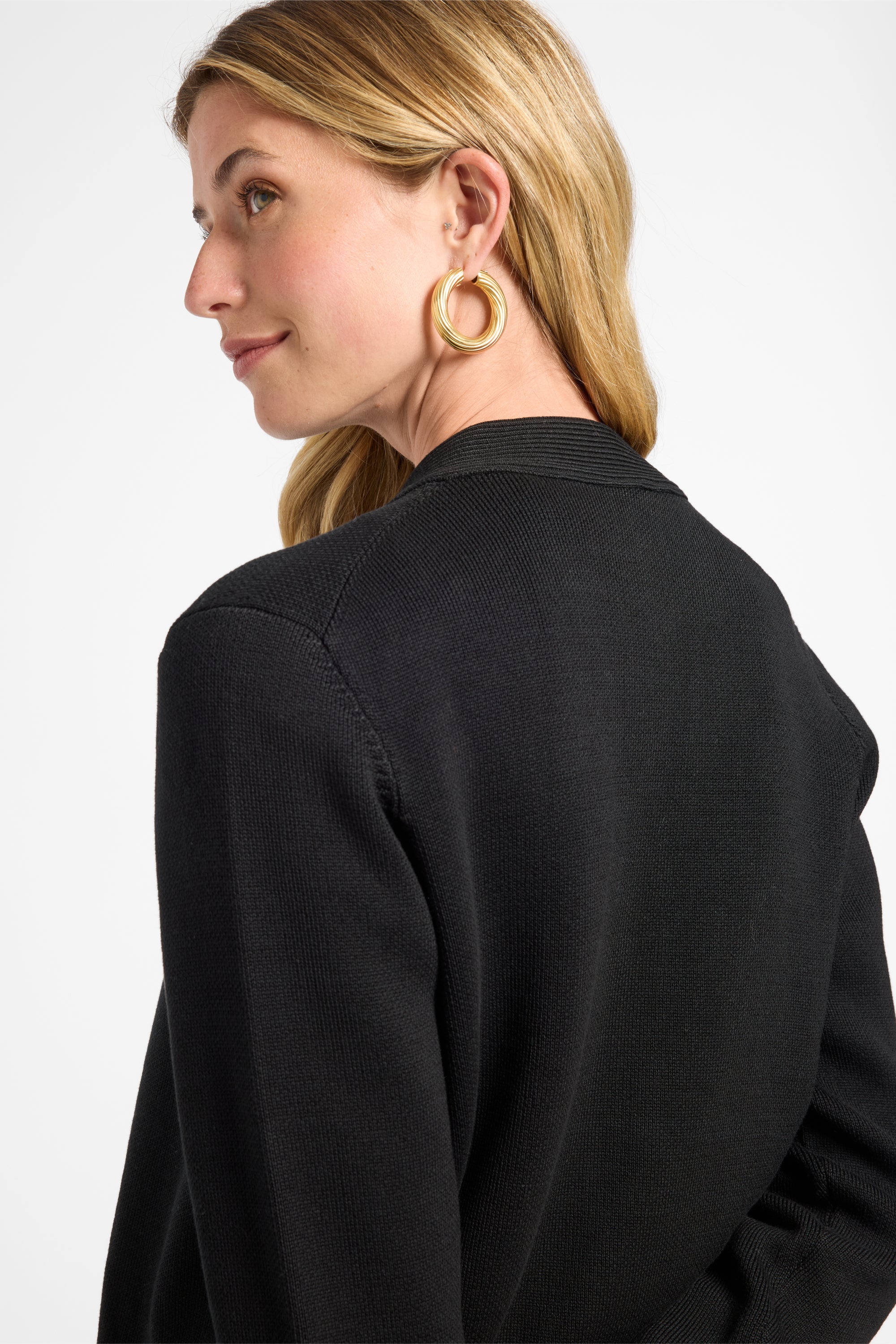 Woman wearing a black cardigan and gold jewelry with a plain background