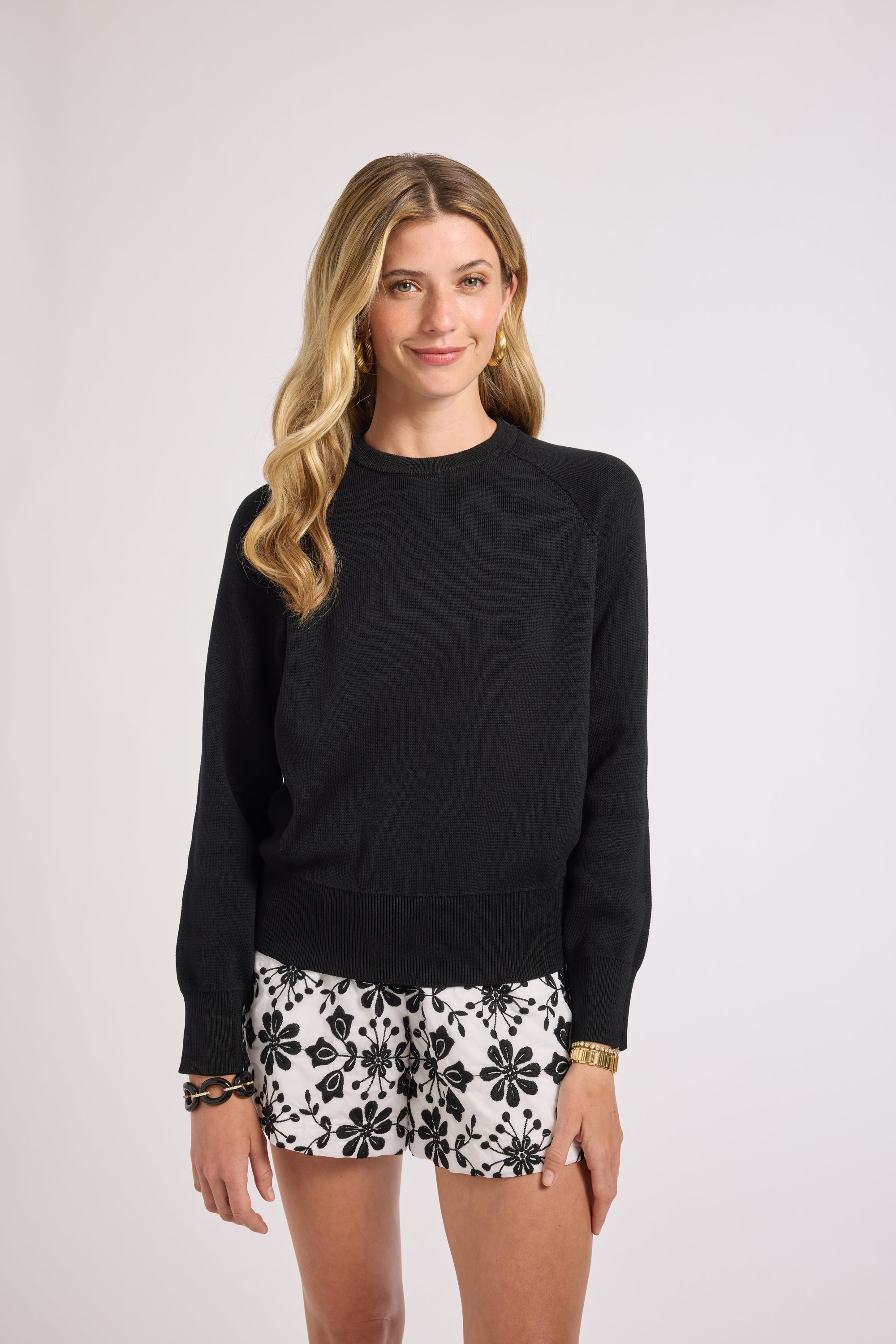 Woman wearing a black crewneck sweater and floral shorts on a white background