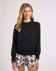 Woman wearing a black crewneck sweater and floral shorts on a white background