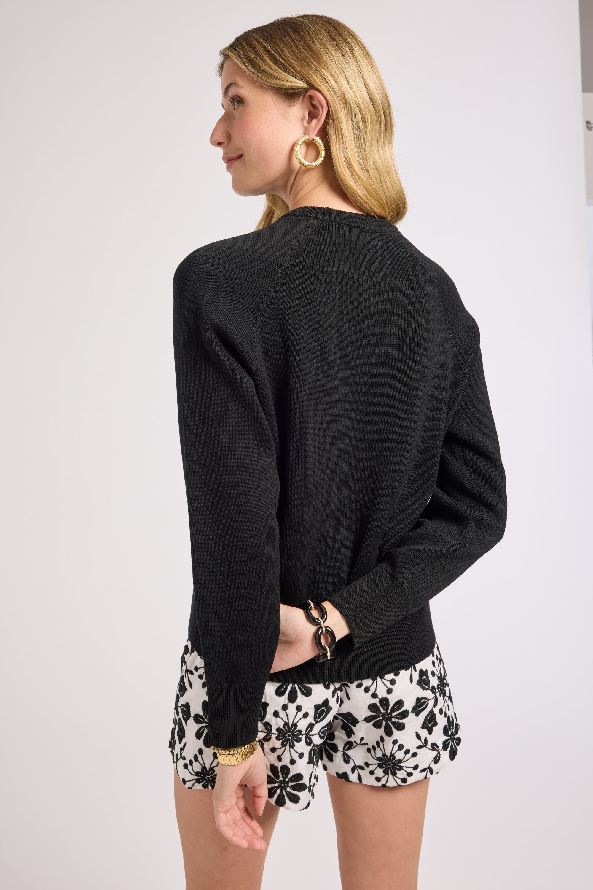 Woman wearing a black crewneck and floral shorts on a plain background