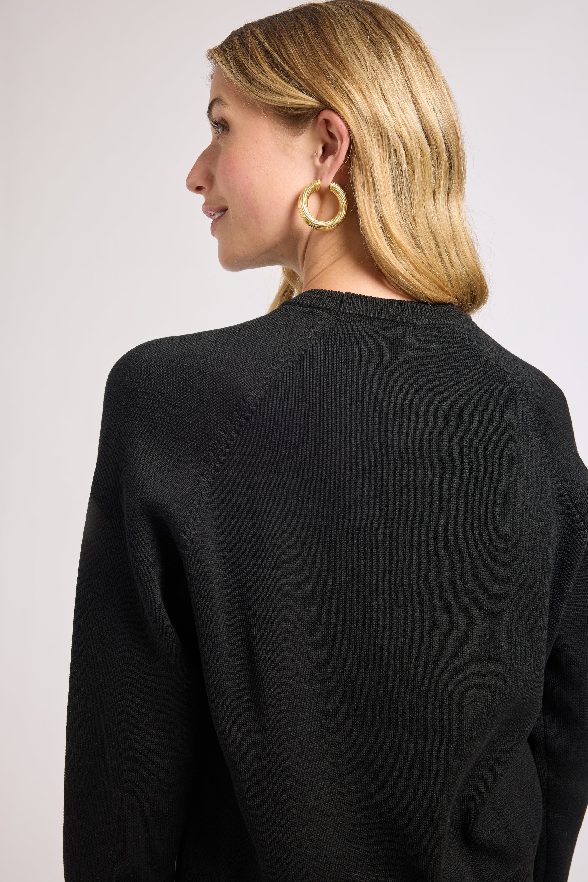 Woman wearing a black long sleeve sweater with a plain background
