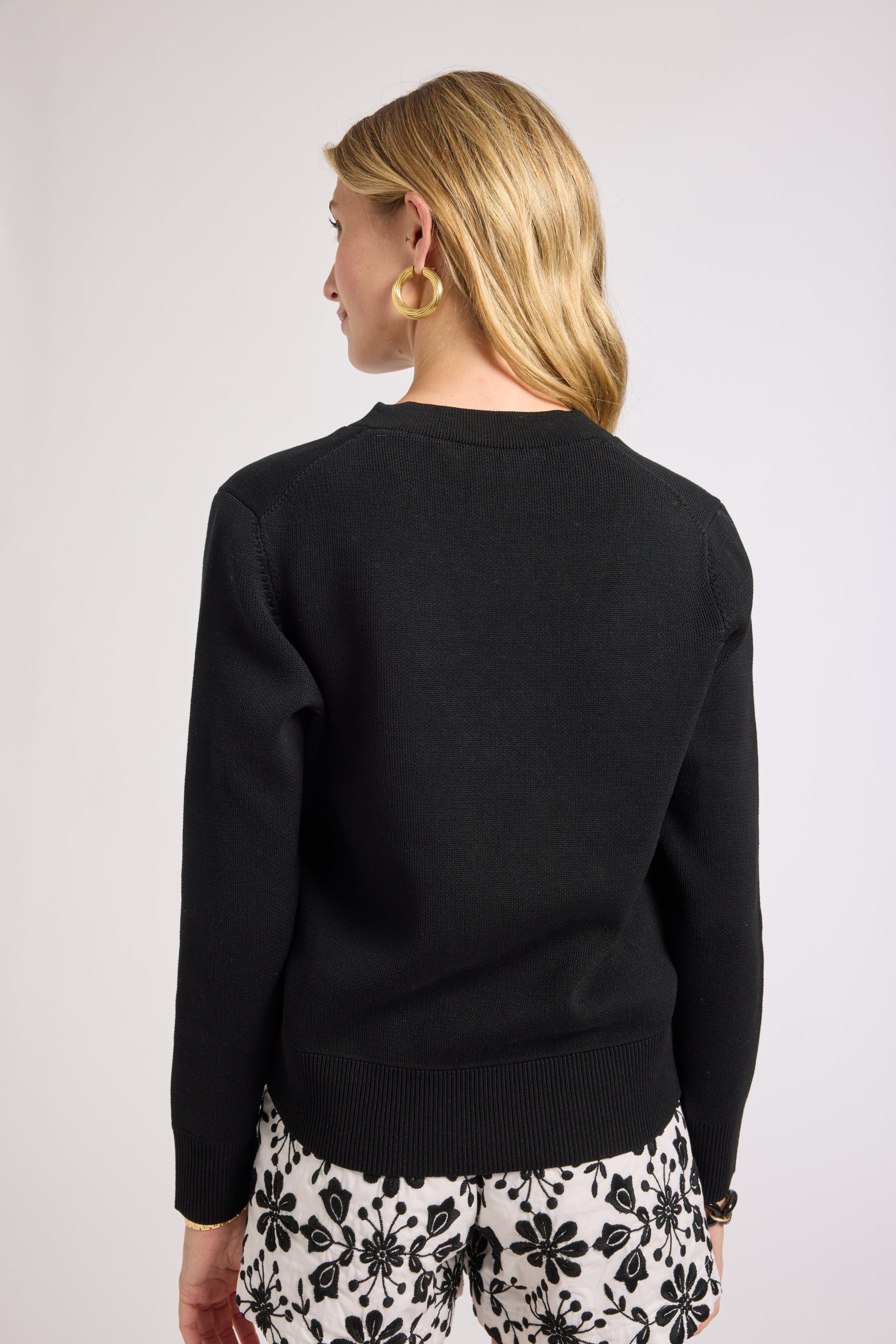 Woman wearing a black sweater with floral shorts on a plain background