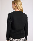 Woman wearing a black sweater with floral shorts on a plain background