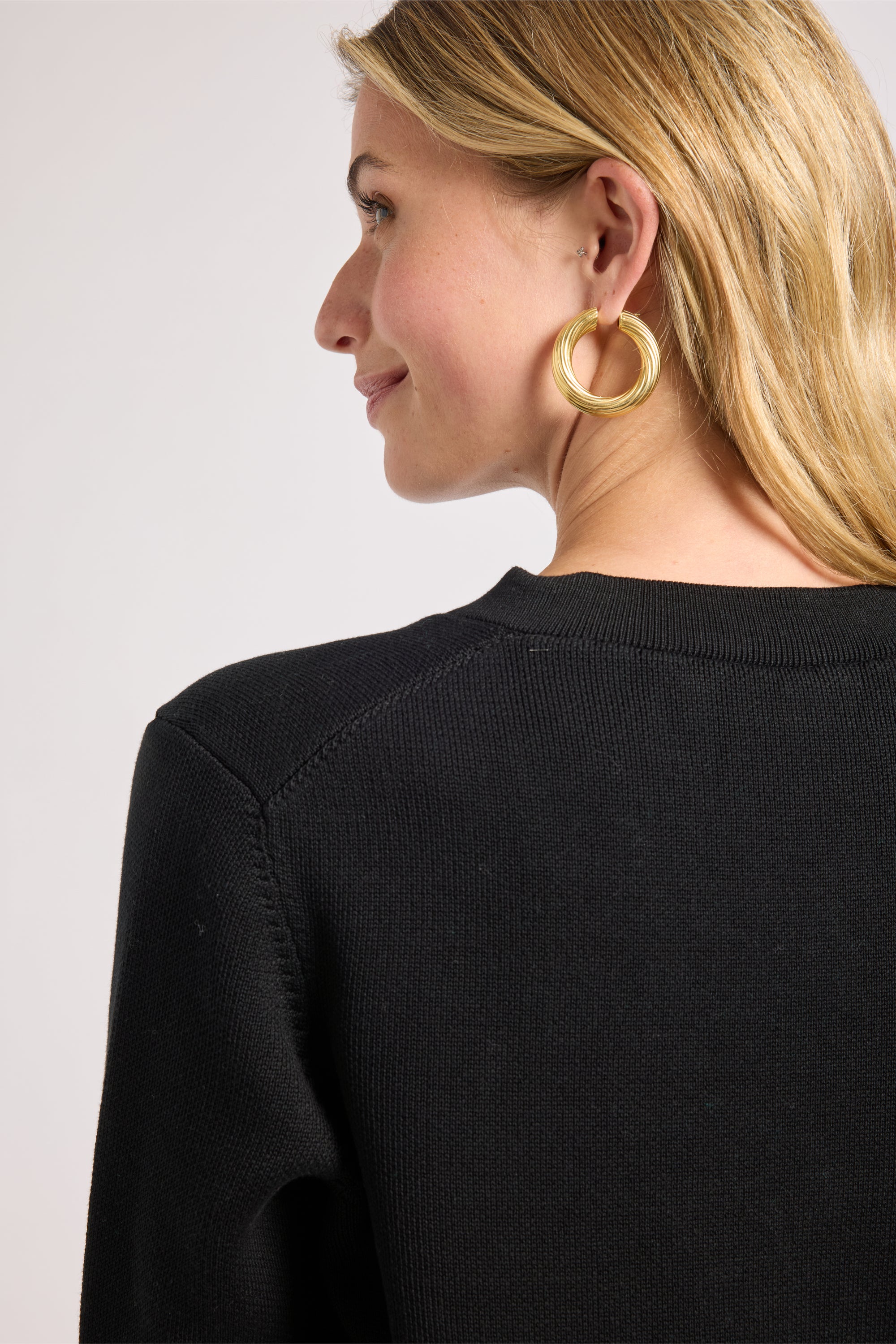 Woman wearing a black sweater and gold earrings with a plain background