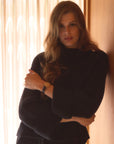 Woman standing in a house wearing the black turtleneck cashmere sweater 