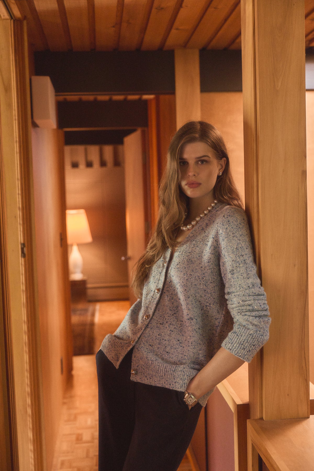 Woman in a home wearing a blue cardigan with a pearl necklace
