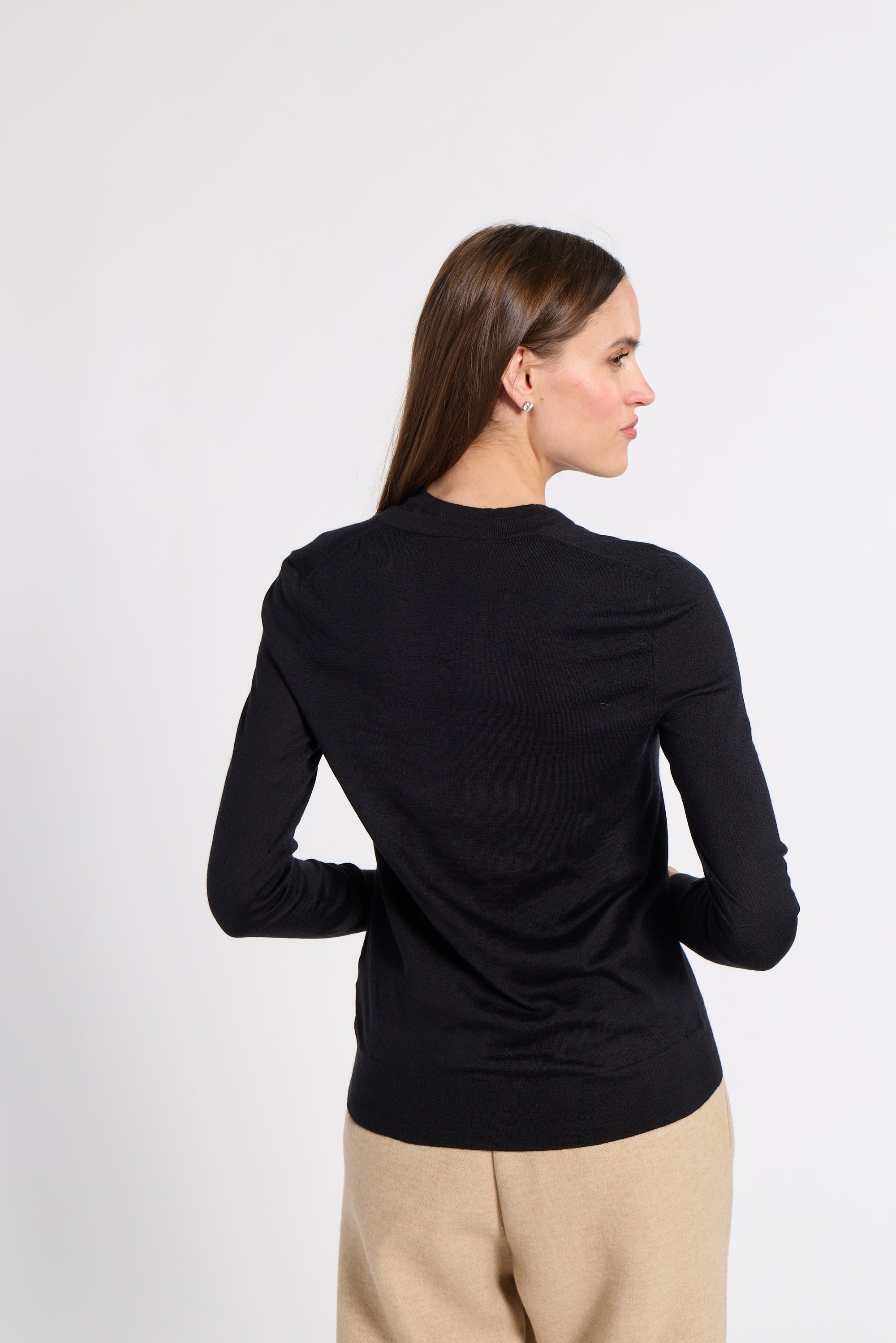 A woman shown from the back wearing a black long-sleeve cardigan top and beige trousers, standing against a light gray studio background.