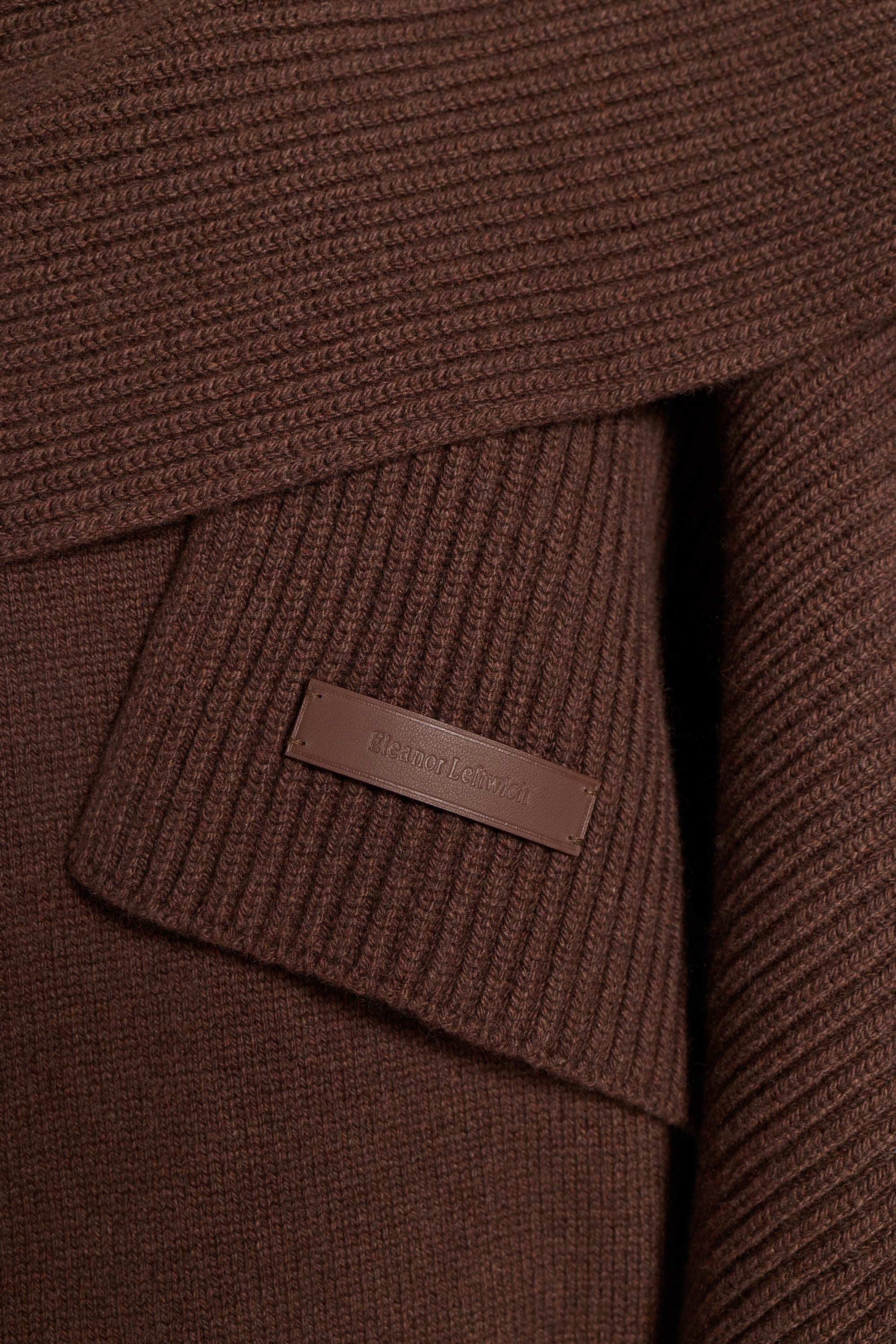 Close-up of a brown ribbed knit garment with a small rectangular leather brand tab reading Barbour.